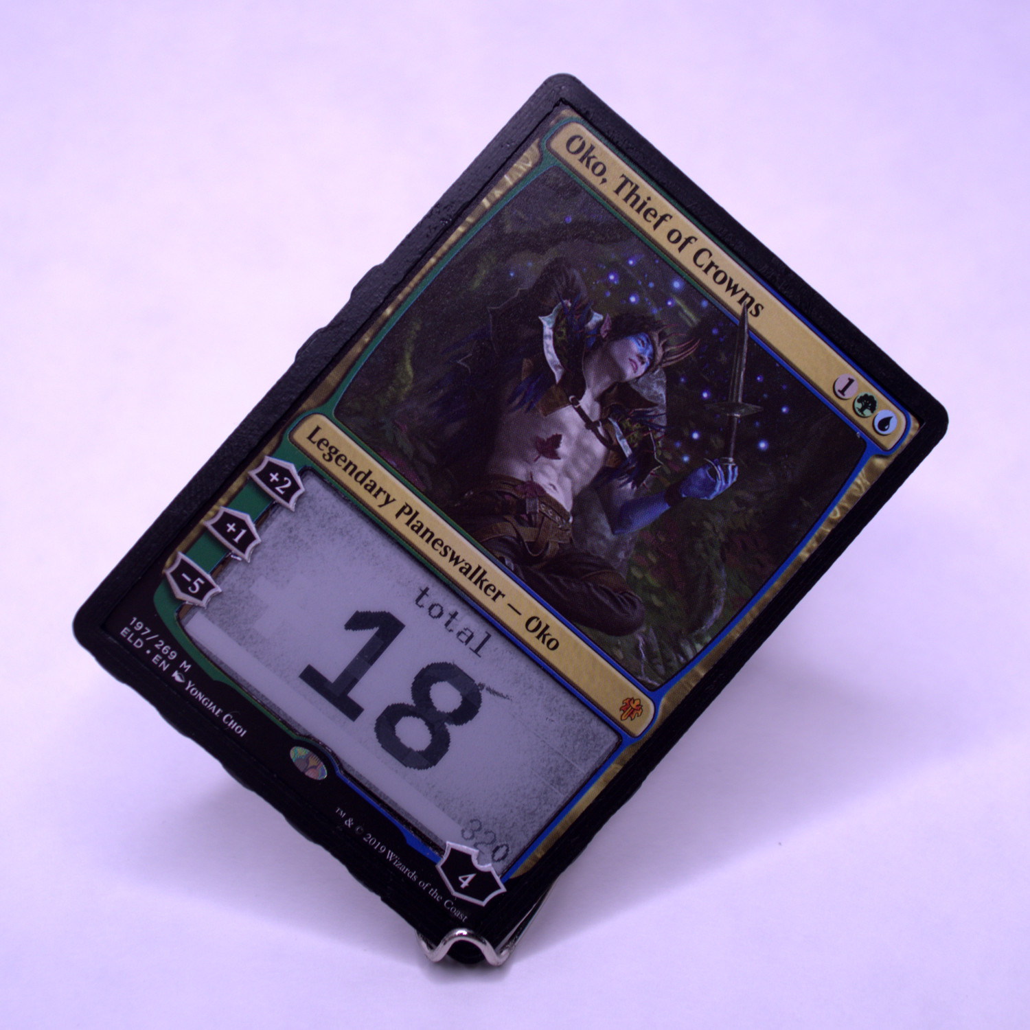 A life counter on a stand that orients it diagonally, seen from the front, showing the Oko, Thief of Crowns card
	and an e-ink display through a cutout where the rules text used to be